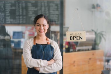 Tezgahta duran kendinden emin kadın baristanın portresi. Önlüklü kadın kafe sahibi kameraya bakıyor ve misafirleri ağırlarken gülümsüyor.