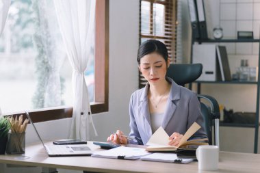 Modern bir ofisteki satış verilerini analiz etmek için dijital tablet kullanan gülümseyen, genç, güzel, profesyonel ve kendinden emin Asyalı bir iş kadınının portresi.