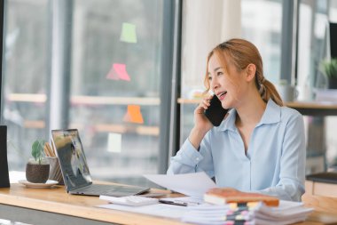Genç Asyalı iş kadını, sekreter, satış müdürü, iş danışmanı, ofisteki bir müşteriyle telefon görüşmesi yapıyor.