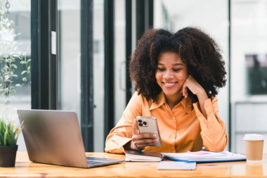 Afro saçlı Afrikalı iş kadını veya muhasebeci pazar verilerini, bilançolarını, hesaplarını ve net kârlarını analiz etmek için hesap makinesi, grafik ve grafikler kullanıyor.