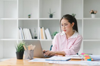 Modern bir ofisteki satış verilerini analiz etmek için dijital dizüstü bilgisayar kullanan gülümseyen, genç, güzel, profesyonel ve kendine güvenen Asyalı bir iş kadınının portresi.