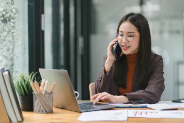 Modern bir ofisteki satış verilerini analiz etmek için dijital tablet kullanan gülümseyen, genç, güzel, profesyonel ve kendinden emin Asyalı bir iş kadınının portresi.