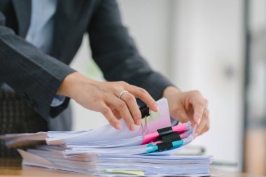 İş kadınının elleri, dağınık ofis masasındaki dosyalar ve dosyalar arasında tamamlanmamış belgeleri aramak ve kontrol etmekle meşguldür.