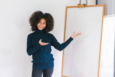 Kameraya gülümseyen ve beyaz tahtayı gösteren güzel Afro-Amerikan kadının stüdyo portresi.