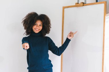 Kameraya gülümseyen ve beyaz tahtayı gösteren güzel Afro-Amerikan kadının stüdyo portresi.