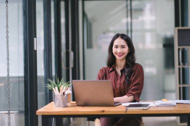 Asyalı bir iş kadını dizüstü bilgisayar kullanıyor ve hesap makinesi ve belgelerle çalışıyor, yatırımlar için mali planlama yapıyor ve mali raporu analiz ediyor
