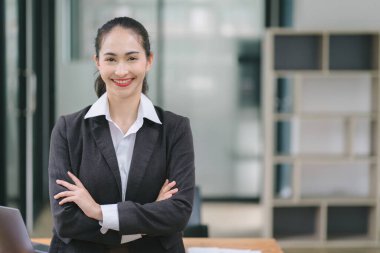 Modern ofiste kesişen kameraya gülümseyen kendine güvenen genç iş kadını portresi.