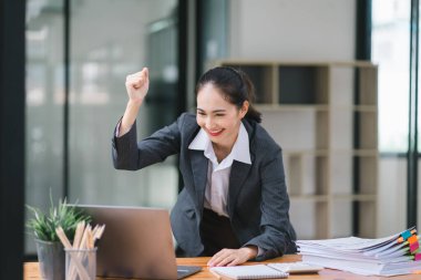 Başarıyı kutlayan genç bir iş kadınının portresi dizüstü bilgisayarın önünde kaldırılmış, yumrukları sıkılmış. Serbest Çalışan bir projeyi tamamladı.