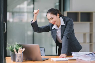 Başarıyı kutlayan genç bir iş kadınının portresi dizüstü bilgisayarın önünde kaldırılmış, yumrukları sıkılmış. Serbest Çalışan bir projeyi tamamladı.
