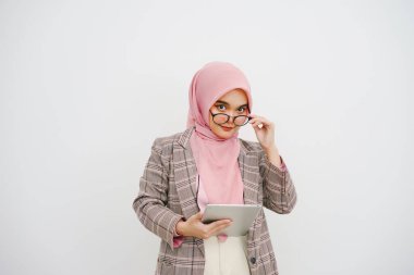 Mutlu, genç, güzel, Müslüman bir iş kadınının portresi pembe tesettür, gözlüklü şirket çalışanı, gülümseyen ve dijital tablet tutan, beyaz arka planda duran