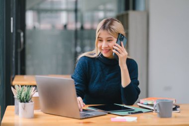 Genç Asyalı iş kadını, sekreter, satış müdürü, iş danışmanı, ofisteki bir müşteriyle telefon görüşmesi yapıyor.
