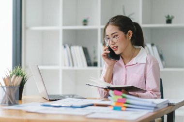 Ofiste cep telefonu ve laptopla çalışan Asyalı güzel sekreterin portresi.