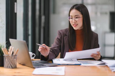 Piyasa verilerini, bilançolarını, hesaplarını ve net kârlarını analiz etmek için hesap makinesi, grafik ve grafikler kullanan Asyalı iş kadını veya muhasebeci