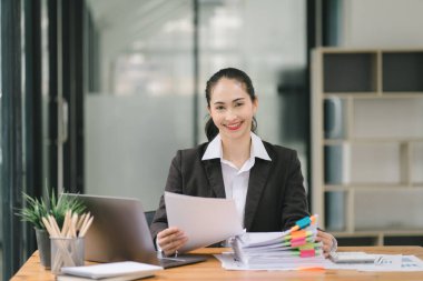 Piyasa verilerini, bilançolarını, hesaplarını ve net kârlarını analiz etmek için hesap makinesi, grafik ve grafikler kullanan Asyalı iş kadını veya muhasebeci