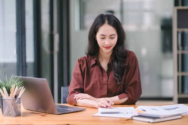 stock image Asian businesswoman or accountant using a calculator, graphs, and charts to analyze market data, balance sheets, accounts, and net profits