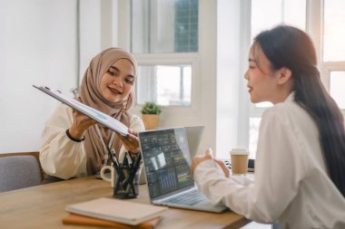 Ofiste finans piyasası verileri ve karşılaştırmaları tartışan iki çok ırklı kadın ofis çalışanı