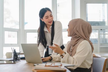 Ofiste finans piyasası verileri ve karşılaştırmaları tartışan iki çok ırklı kadın ofis çalışanı