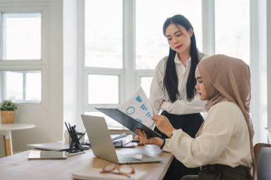 Ofiste finans piyasası verileri ve karşılaştırmaları tartışan iki çok ırklı kadın ofis çalışanı