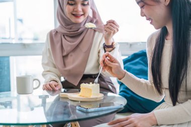 İki çoklu etnik arkadaş bir kafede kahve ve kekin tadını çıkarıyor, sohbet ediyor ve gülüyorlar.