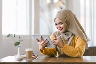 Asyalı Müslüman iş kadını içeride çalışırken dijital tablet kullanıyor.