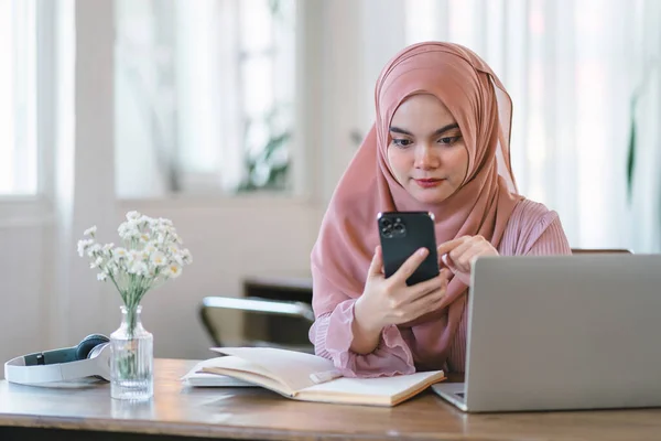 Stock image Asian muslim business woman wearing hijab using phone while working at computer in office