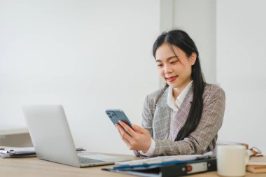 Asyalı iş kadını mutlu ve neşeliyken akıllı telefonlar kullanıyor ve çalışıyor. Genç iş kadını cep telefonlarında uygulamalar kullanıyor, haberleri okuyor.