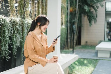 Bir kafede rahat bir atmosferde kahve içip cep telefonu kullanan Asyalı girişimci kadınlar.