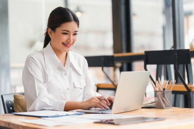 Beautiful asian businesswoman smiling while working with laptop computer at a Modern Co working Space. Remote work concept