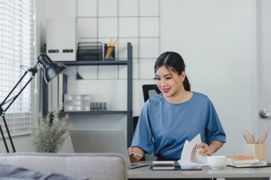Focused young Asian businesswoman sitting and remote working on a computer in a modern home office. Distant workday concept