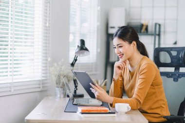 Focused young Asian businesswoman sitting and remote working on a computer in a modern home office. Distant workday concept