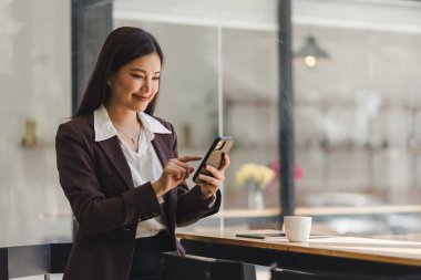 Beautiful young millennial Asian woman using a smartphone at a cafe. Portrait of a gorgeous smiling female engrossed in her mobile phone