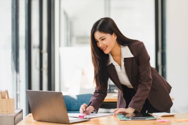 Gülümseyen Asyalı kadın ofis çalışanı dijital bilgisayarla toplantı odasında çalışıyor.