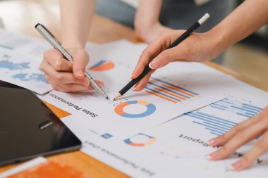 Bir ofiste istatistiksel bir rapor hazırlayıp mali verileri tartışan iki işadamı veya bir pazarlama ekibi, dizüstü bilgisayar ekranında veri tabloları, grafikler ve bir gösterge panelini inceliyor.