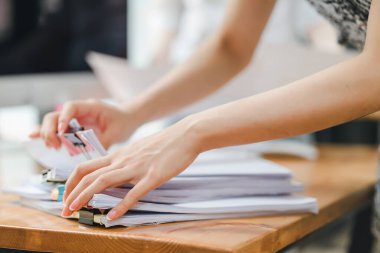 Ahşap bir masa üzerinde renkli cilt klipsleri olan bir yığın belgeyi düzenleyen ellerin yakın çekimi