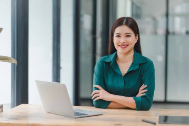 Modern ofiste dizüstü bilgisayar kullanan kendinden emin Asyalı genç bir iş kadını.