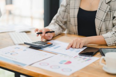 İşadamı, bir hesap makinesi ile bütçeyi hesaplıyor ve ahşap bir masadaki belgelerin finansal çizelge ve grafiklerini analiz ediyor..