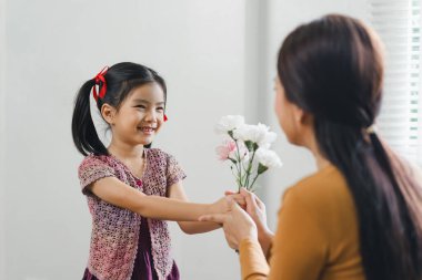 Anneler günün kutlu olsun. Anneler gününde, rahat bir oturma odasında annesine çiçek veren genç bir kız..