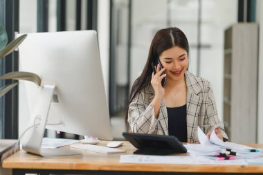 Meşgul profesyonel iş kadını ofis çalışma alanındaki masaüstünü kullanırken bir telefon görüşmesi yapıyor