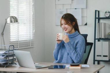 Modern bir ofis molasında sıcak bir içeceğin keyfini çıkaran gülümseyen genç bir kadın.