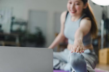 Genç Asyalı kadın açık dizüstü bilgisayarın önünde egzersiz yapıyor. Profesyonel online fitness eğitmeninin talimatlarını tekrarlıyor..