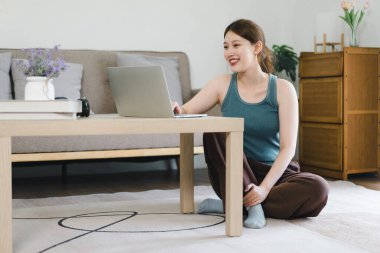 Gündüz vakti evde dizüstü bilgisayarda çalışan genç bir kadın.