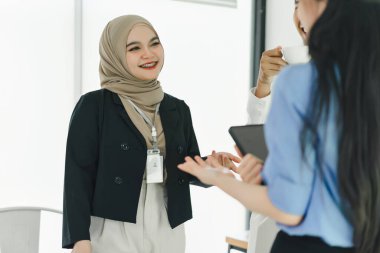 Toplantı molası sırasında modern bir ofiste arkadaşça sohbet eden meslektaşlar.