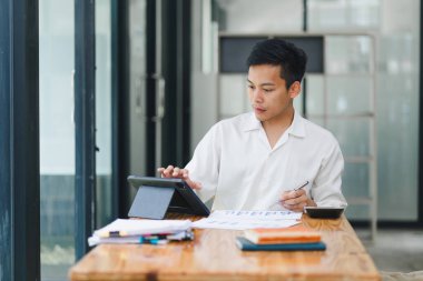 Parlak ofiste tablet üzerinde çalışan genç adam.