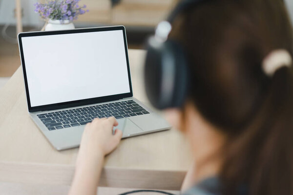 Woman wearing headphones working on laptop in modern home office. The laptop screen is blank for graphic montage
