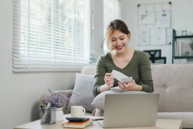Mutlu Asyalı genç iş kadını vergileri hesaplıyor, yerli faturaları sayıyor, e-bankacılık, e-ticaret, evde hesaplama için dizüstü bilgisayar kullanıyor..