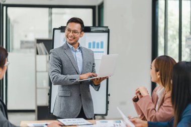 Gri takım elbiseli bir işadamı modern bir ofiste grafikler ve grafiklerle sunumu yönetiyor..