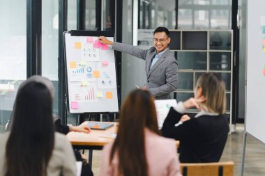 İş adamı, bir ofis toplantısı sırasında ilgili bir ekibe veri ve çizelge sunuyor, işbirliği ve tartışmayı teşvik ediyor.