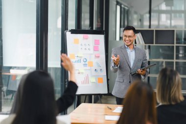 İş adamı, bir ofis toplantısı sırasında ilgili bir ekibe veri ve çizelge sunuyor, işbirliği ve tartışmayı teşvik ediyor.