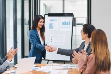 İş arkadaşları el sıkışıyor ve modern bir ofiste başarılı bir sunumu kutluyorlar.