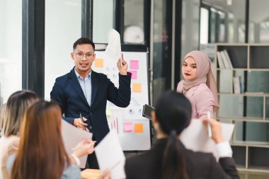 Çeşitli iş adamları ofis toplantısı sırasında verileri analiz ediyor ve stratejileri tartışıyor, belgeler ve dizüstü bilgisayar kullanarak.